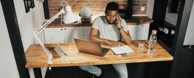 Absenteeism in Distributed Teams: Portrait of young African-American man wearing glasses while working from home and using laptop.