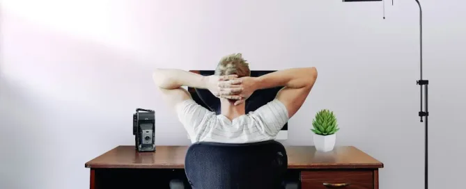 Low Code Development: relaxed man holding his head while sitting on a chair facing the computer