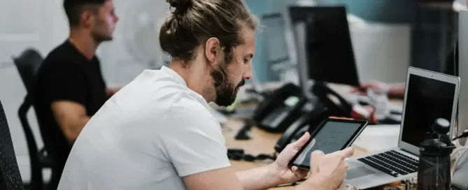 tech talent retention: man holding turned-on iPad in front of turned-off MacBook Air