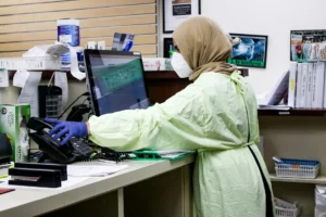 Types of Health-Oriented Software: Photo of woman in green scrubs updating patient data in computer