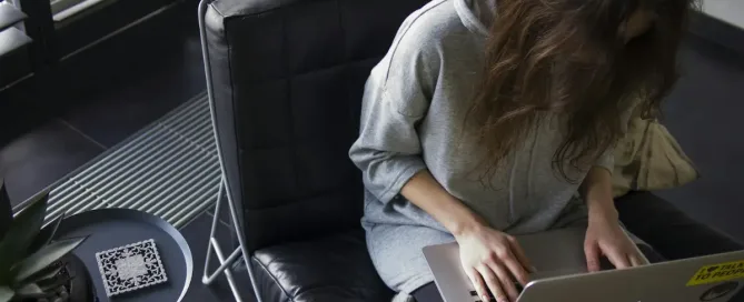 api security: woman in blue chambray long-sleeved top sitting on black leather chair with silver MacBook on lap