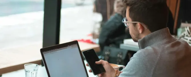 Mistakes When Hiring Software Developers; man sitting near table with laptop and smartphone near window