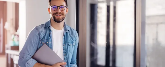 The rise of green software prioritizes minimizing the environmental footprint of software throughout its lifecycle. in the photo a software developer stands in a hallway, holding a closed laptop