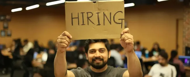 Man holding a bright sign that reads "Hiring," symbolizing attracting talent through employer branding and talent marketing.