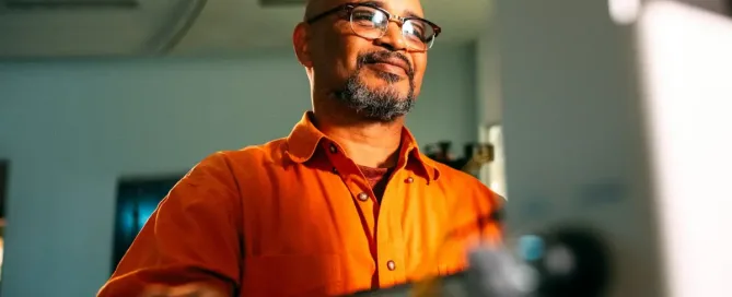 Agile Nearshore Development: man in orange shirt smiles at screen as he moves the mouse