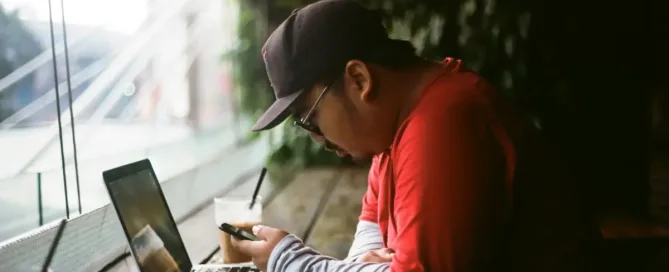 Cultural Sensitivity: man holding phone in with laptop beside cup