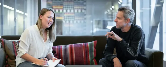 Pivot, Patch, or Persevere: woman in white long sleeve shirt sitting on red couch, discussing with grey-haired man using dark outfit