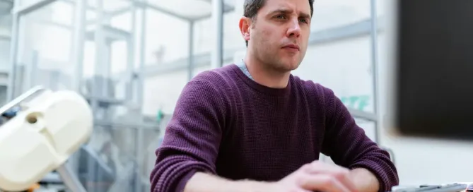 Virtual Team Management Challenges: man in purple sweater sitting at the table using computer and looking worried