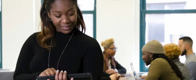 data representation: a woman standing in front of a table full of people, reading at a tablet