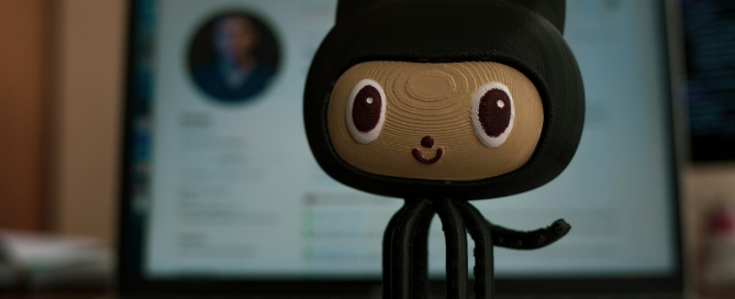 mona the octocat: A figurine of an oktokat in the center, in the background a laptop with the main page of the GitHub open.