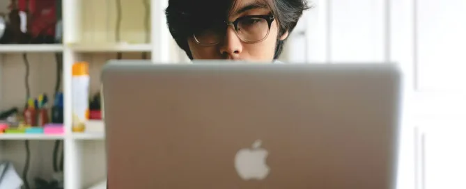 version control systems: man wearing eyeglasses while using silver Macbook near wooden cubby shelf inside room