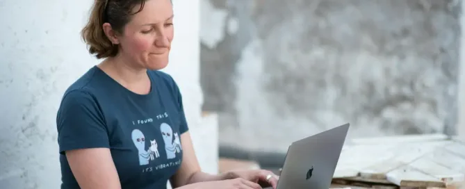 aws engineers: Woman working on a laptop on the outdoor terrace on a roughly made wooden table and a tech book in the background