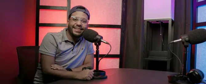 tech podcast guide: man wearing glasses and baseball cap smiles in front of a professional microphone