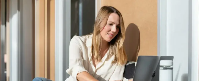 Recruiter's Personal Brand on LinkedIn: woman in white long sleeve shirt and blue denim jeans sitting on brown wooden table using laptop in the sun