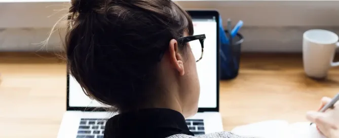 offer letter template: young woman with a hair in a bun takes notes while looking at computer