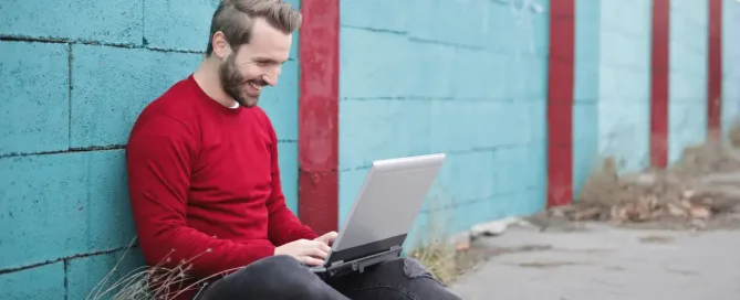 team leadership: man sitting on the ground smiling at laptop