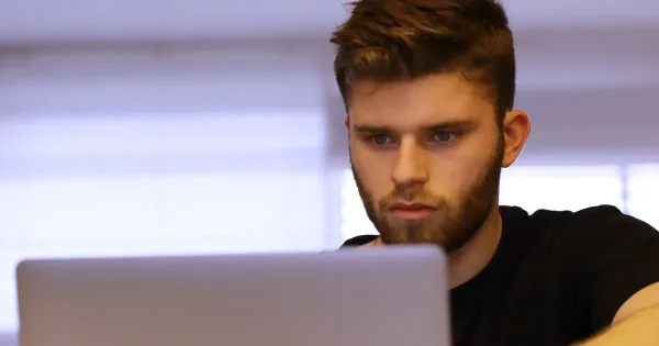 devops tools: young man in dark t-shirt leans toward laptop computer screen