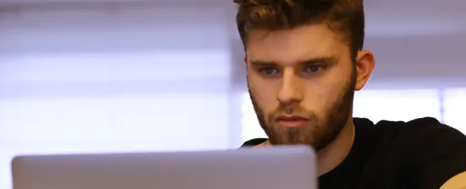 devops tools: young man in dark t-shirt leans toward laptop computer screen