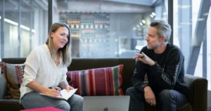 Pivot, Patch, or Persevere: woman in white long sleeve shirt sitting on red couch, discussing with grey-haired man using dark outfit