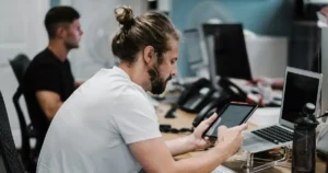 tech talent retention: man holding turned-on iPad in front of turned-off MacBook Air