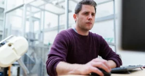 Virtual Team Management Challenges: man in purple sweater sitting at the table using computer and looking worried