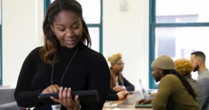 data representation: a woman standing in front of a table full of people, reading at a tablet