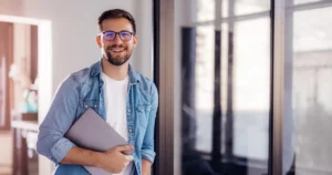 The rise of green software prioritizes minimizing the environmental footprint of software throughout its lifecycle. in the photo a software developer stands in a hallway, holding a closed laptop