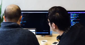 software interrupts: Computer programmer takes a look at colleague's laptop to review the programming code on the screen.